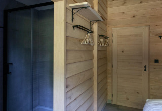 Interior revestido de madera con estante, perchas y ducha de cristal en una cabaña en Bélgica.
