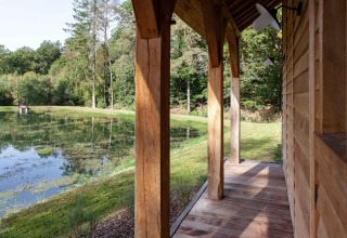 Træveranda udsigt over rolige dam og skov ved lodge Cabane The Funny Friends i Belgien.