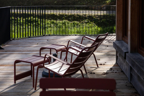Deck with red lounge chairs and footrests at Cabane 'The Funny Friends' lodge in Belgium, sunlit setting.