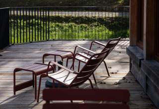 Deck with red lounge chairs and footrests at Cabane 'The Funny Friends' lodge in Belgium, sunlit setting.