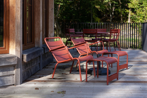 Outdoor terrace at Cabane The Funny Friends in Belgium with red chairs and tables beside a wooden lodge.