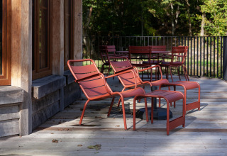 Outdoor terrace at Cabane The Funny Friends in Belgium with red chairs and tables beside a wooden lodge.