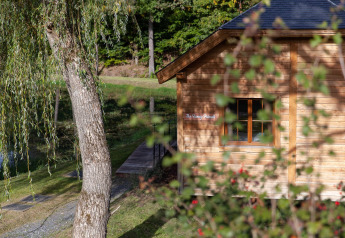 Houten hut genaamd 'The Funny Friends' in België, deels verborgen achter takken, in een groene omgeving.