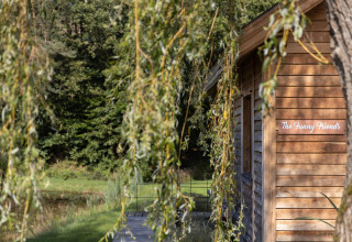 Cabaña de madera llamada 'The Funny Friends' en Cabane, Bélgica, rodeada de naturaleza y vegetación.