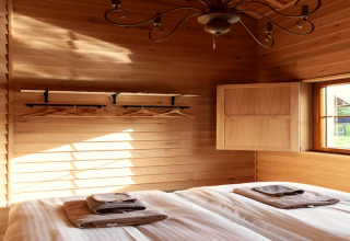 Camera da letto in legno illuminata, lodge 'Happiness', Belgio, letto matrimoniale, asciugamani e finestra.