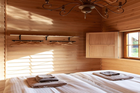 Bright wooden bedroom at lodge 'Happiness', Belgium, with bed, towels, coat rack and sunlight.