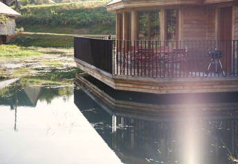 Chalet in legno sul lago con terrazza e sedie, riflessi sul lago presso il Lodge Happiness in Belgio.