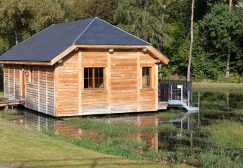 Il lodge in legno 'Happiness' sorge accanto a uno stagno in una tranquilla foresta belga.