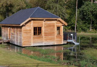 A cozy wooden lodge named 'Happiness' is situated beside a pond in a serene Belgian forest.