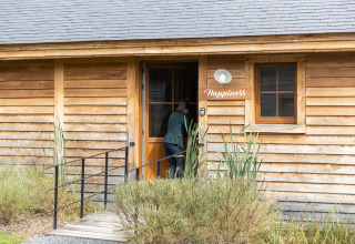 Person entering a wooden lodge named 'Happiness' with plants in front, photo taken in Belgium.