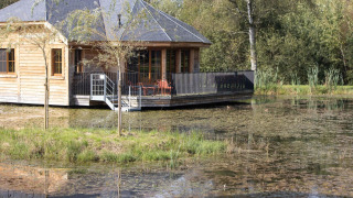 Een houten lodge genaamd Happiness staat aan de vijver, omringd door natuur en groene vegetatie.