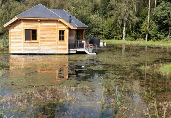 Lodge di legno chiamato 'Happiness' su uno stagno in Belgio, circondato dalla natura e riflesso nell’acqua.