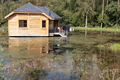 Wooden lodge named 'Happiness' on a pond in Belgium, surrounded by nature with reflection in the water.