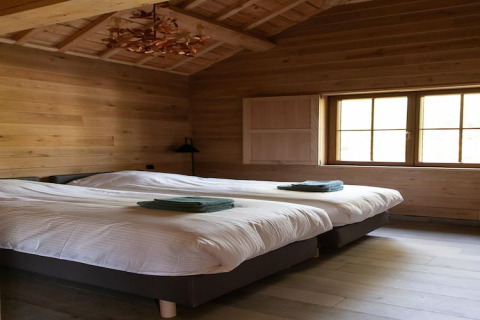 Room at lodge ‘Happiness’ in Belgium featuring two single beds, wooden walls, and sunlight through window.