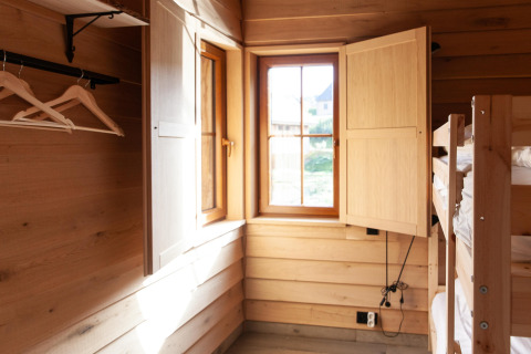 Interior of a wooden lodge named ‘Happiness’ in Belgium with bunk beds, open window, and hangers.