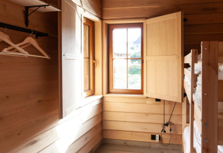 Interior of a wooden lodge named ‘Happiness’ in Belgium with bunk beds, open window, and hangers.