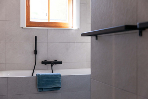 Modern bathroom with bathtub, black fixtures, a blue towel, and window at Lodge Happiness in Belgium.