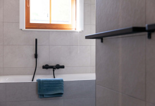Modern bathroom with bathtub, black fixtures, a blue towel, and window at Lodge Happiness in Belgium.