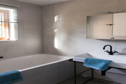 Contemporary bathroom at the Happiness lodge in Belgium featuring a bathtub, sink, mirror, and blue towels.