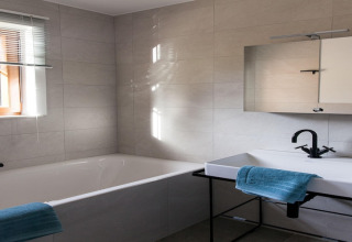 Contemporary bathroom at the Happiness lodge in Belgium featuring a bathtub, sink, mirror, and blue towels.
