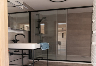 Modern bathroom at lodge 'Happiness' in Belgium featuring a black faucet, sink, and glass shower.
