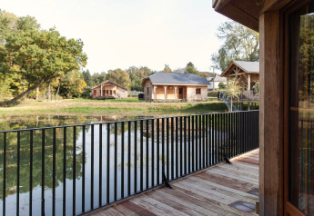 Vista dal balcone del lodge «Happiness» in Belgio su uno stagno, casette in legno e natura circostante.