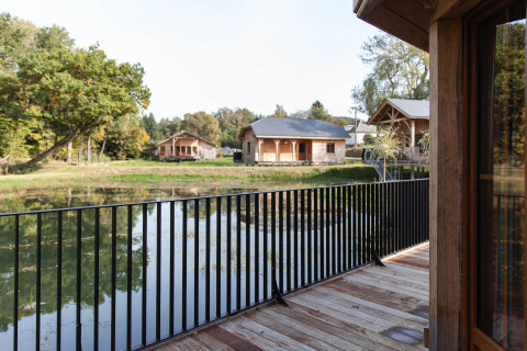 View from a balcony at lodge 'Happiness' in Belgium overlooking a pond, cabins, and wooded scenery.