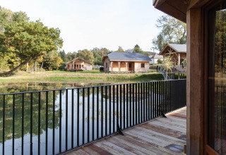 View from a balcony at lodge 'Happiness' in Belgium overlooking a pond, cabins, and wooded scenery.