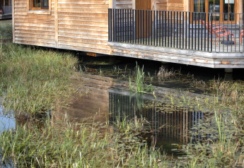 Un lodge in legno su palafitte chiamato “Happiness” in Belgio è riflesso nell’acqua e nell’erba.