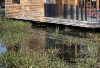 A wooden lakeside lodge called “Happiness” in Belgium, with porch and water reflection in the foreground.