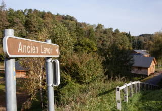 A sign reading 'Ancien Lavoir' points toward a wooden lodge named 'Happiness' in Belgium's greenery.