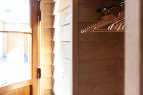 A sunlit wooden wardrobe with empty hangers inside a lodge named «Happiness» in Belgium.