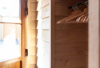 A sunlit wooden wardrobe with empty hangers inside a lodge named «Happiness» in Belgium.