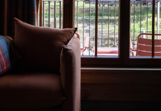 View from a cozy sofa by the window at Lodge ‘Happiness’ in Belgium, showing terrace and greenery.