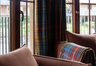 View from the living room at lodge “Happiness” in Belgium, with plaid blanket and green scenery outside.