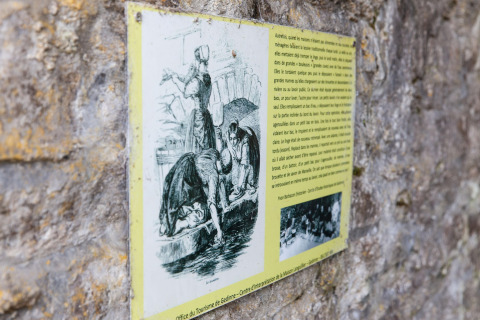 Information plaque on a stone wall, showing women washing clothes, photographed at a lodge in Belgium.