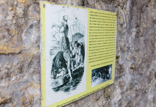Information plaque on a stone wall, showing women washing clothes, photographed at a lodge in Belgium.