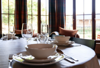 Table set with bowls and glassware in a Belgian lodge named 'Happiness' with bright windows in view.