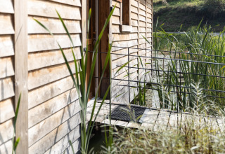 Entrance of the 'Happiness' lodge in Belgium with wooden siding, reeds, and natural pond scenery.