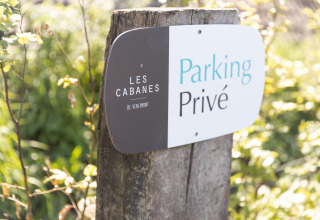 Sign at Les Cabanes de Vencimont, Belgium, reading 'Private Parking' on a wooden post surrounded by greenery.