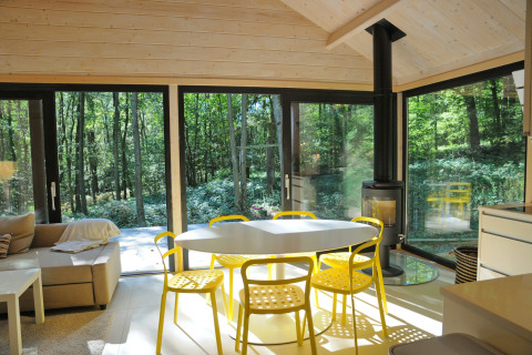 Eethoek in chalet 'Drôles d'écureuil' in België met gele stoelen, veel licht en uitzicht op het bos.