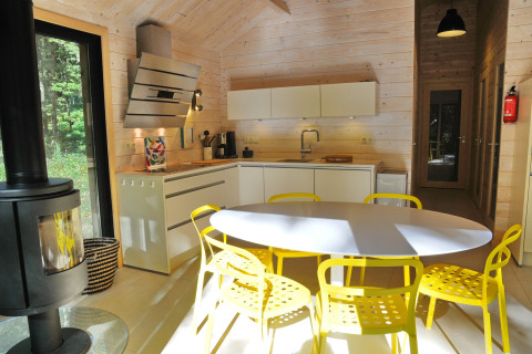 Moderne chaletkeuken in België met gele stoelen, witte kasten en groot raam met uitzicht op het bos.