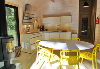 Moderne chaletkeuken in België met gele stoelen, witte kasten en groot raam met uitzicht op het bos.