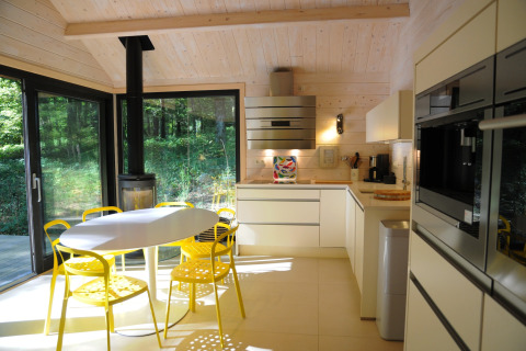 Moderne chaletkeuken met gele stoelen, ronde tafel en grote ramen met uitzicht op het bos in België