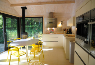 Moderne chaletkeuken met gele stoelen, ronde tafel en grote ramen met uitzicht op het bos in België