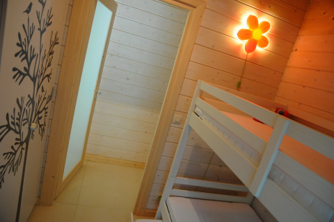 Lichte houten kamer met stapelbed, bloemenwandlamp en boomdecoratie in een chalet in België.
