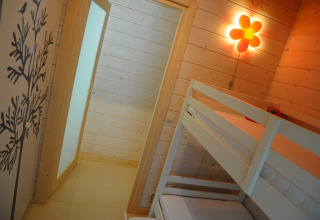 Lichte houten kamer met stapelbed, bloemenwandlamp en boomdecoratie in een chalet in België.