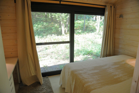 Slaapkamer in chalet ‘Droles d'écureuil’ in België met grote glazen deuren en uitzicht op groen bos.