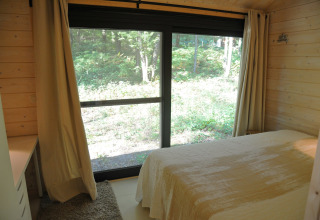 Slaapkamer in chalet ‘Droles d'écureuil’ in België met grote glazen deuren en uitzicht op groen bos.