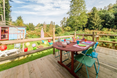 Wooden deck with colorful table setting overlooking nature at Les Roulottes de Vio mobile home in Belgium.